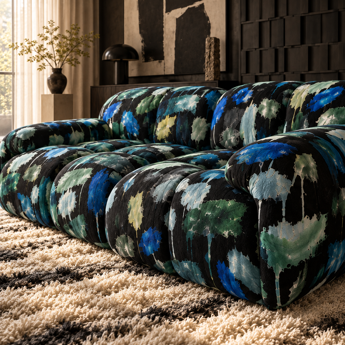 A modern tufted sofa with a bold abstract watercolor-style upholstery pattern in black, blue, green, and cream, styled in a contemporary living room setting on a shag rug.